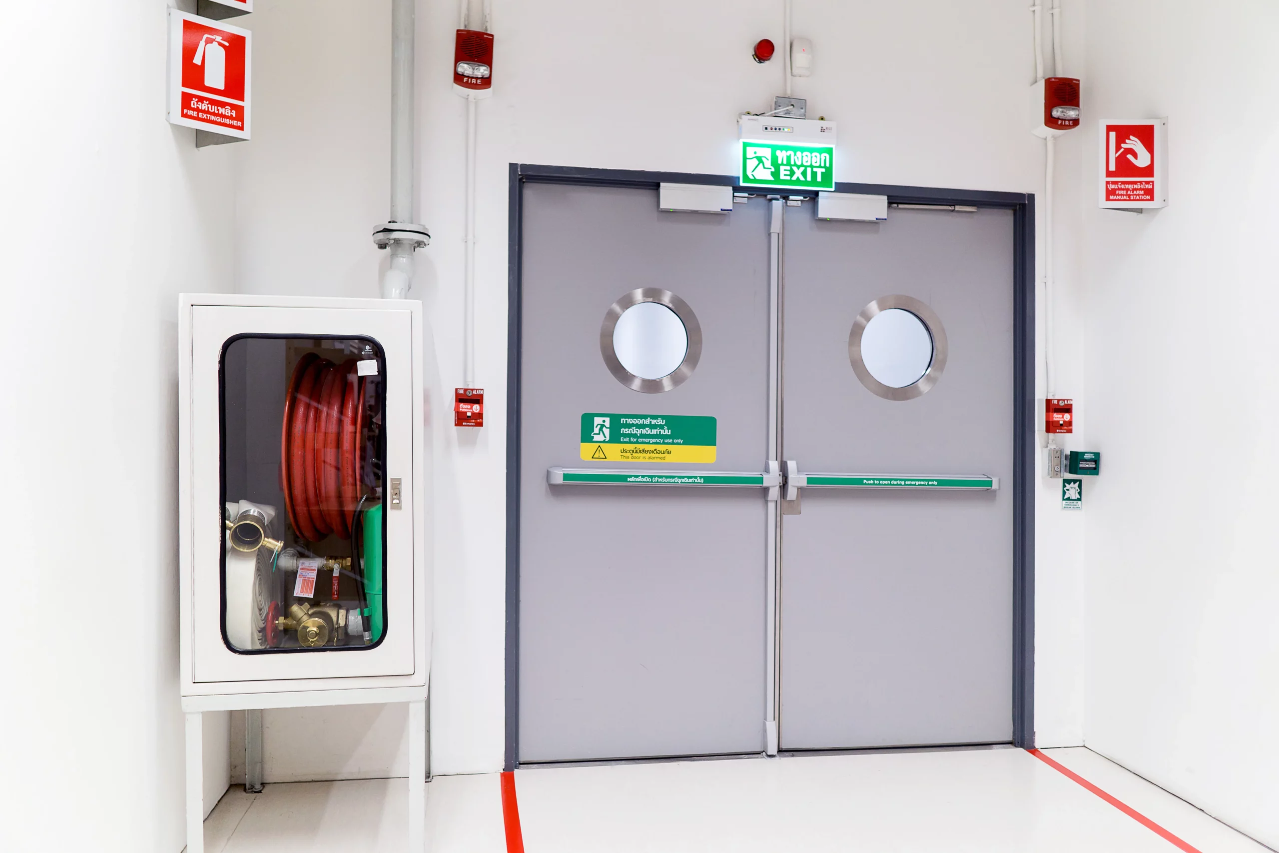 a fire door. exit signs and a water hose. also pictured is a fire extinguisher sign. 