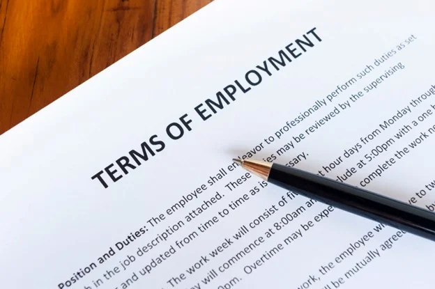 A contract of employment on a wooden table in the process of being signed by the employee and employer.