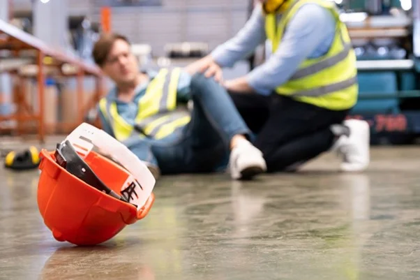 a person who has fallen over, and their hard hat is on the floor next to them. 