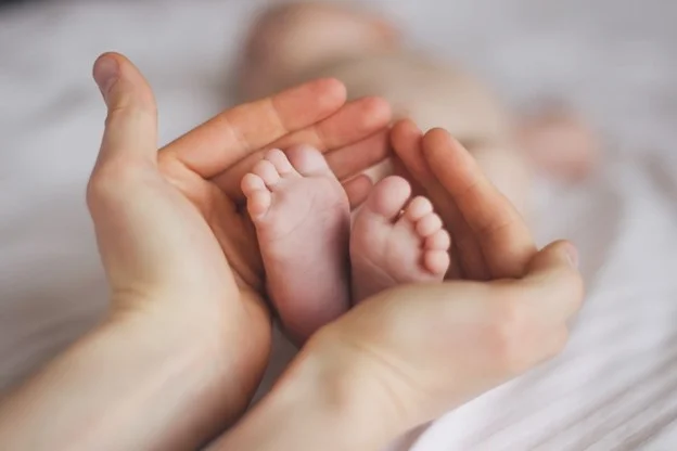 A new mother holding the feet of her baby whilst on maternity leave whilst receiving statutory maternity pay 