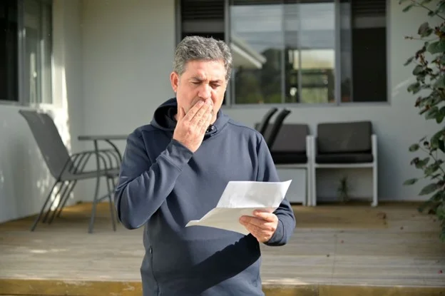 male employee reading a letter of concern regarding poor performance outside their home. 