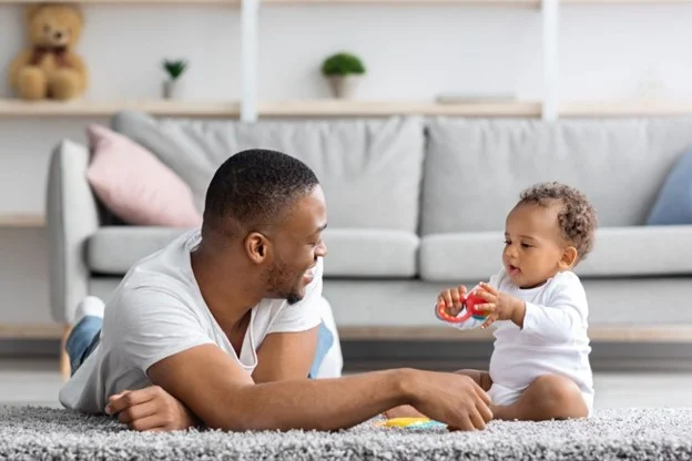 a young day plays with his baby in the living room of their home, whilst on shared parental leave from work. 