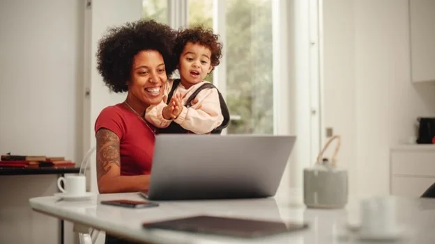 A young mother eligible for shared parental leave through birth or adoption, plans her return to work on her laptop. 