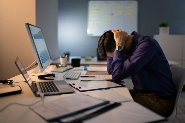 An employee holding their head due to workplace stress caused by an unmanageable workload. 