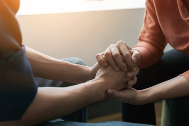 Image focusing on two people holding hands offering support to one another. 